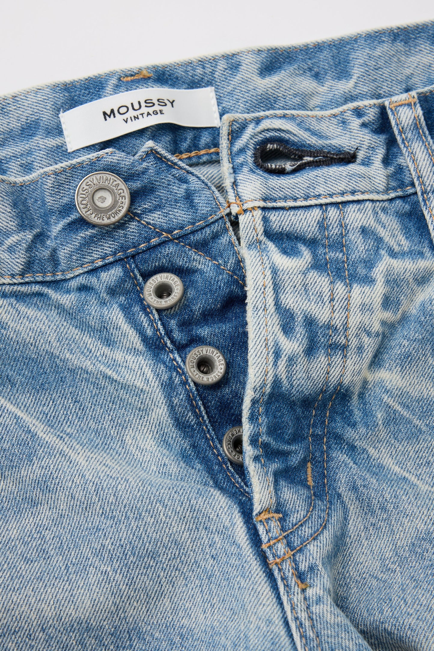 Close-up of light blue low-rise Wildwood Straight Leg Jeans by Moussy, featuring a partially open button fly. They have a faded pattern, contrasting stitching, and are made from responsibly sourced cotton.