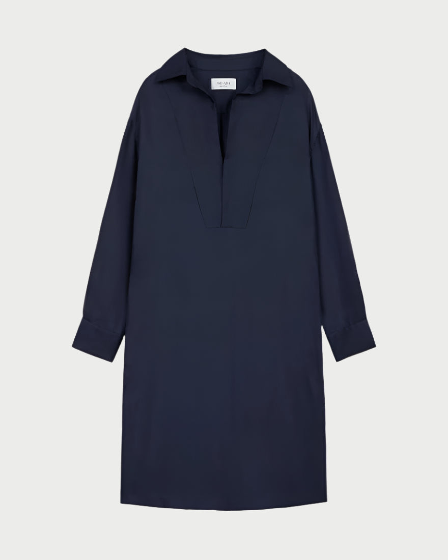 The Society Dress by WE-AR4, a navy blue long-sleeve collared shirtdress made from upcycled silk, features a V-neck design and loose fit. It falls just above the knees and is showcased against a light gray background.