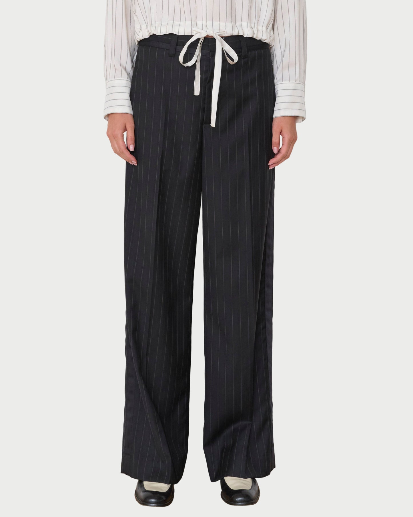 Person wearing black pinstripe pants with a white shirt against a white wall.