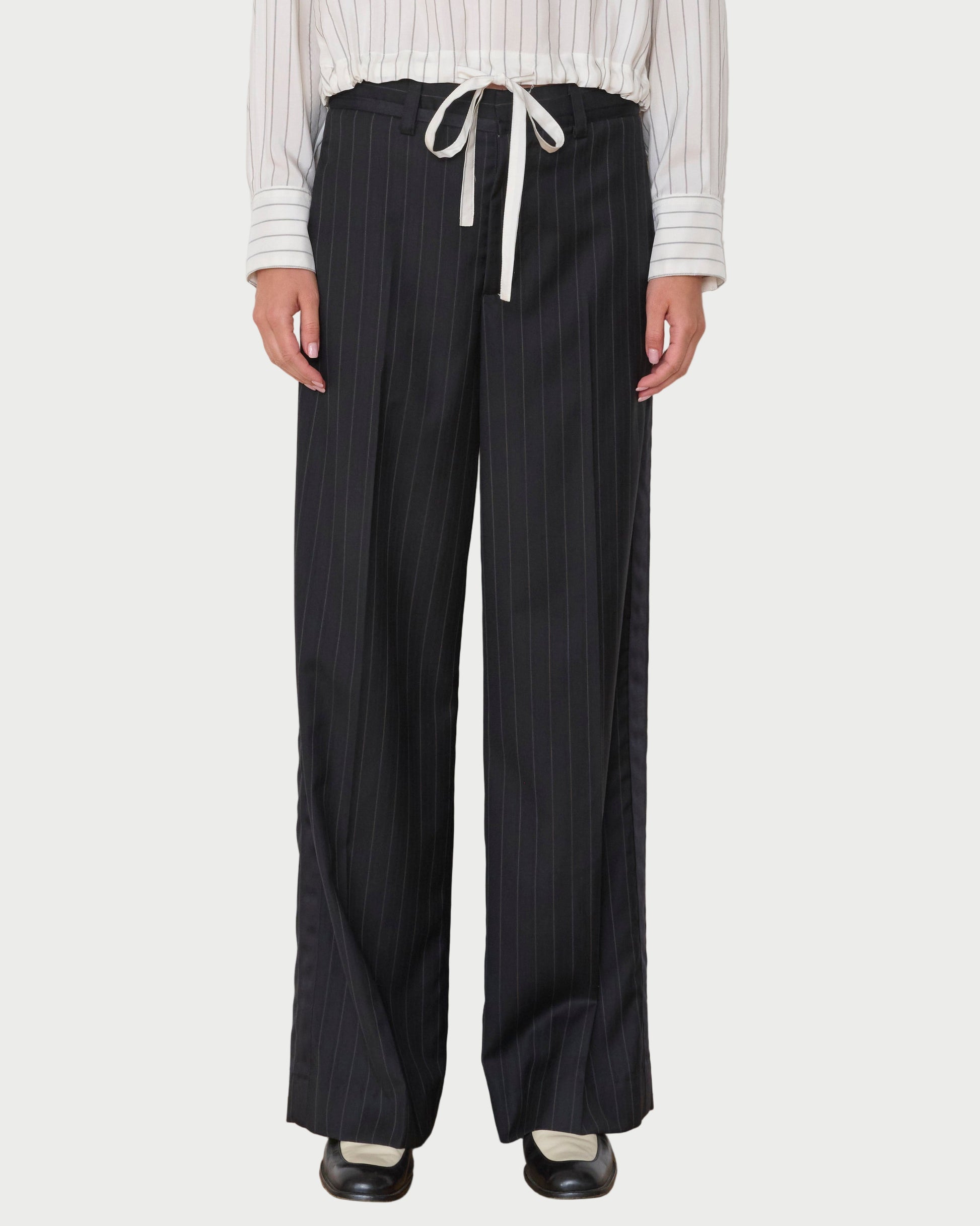 Person wearing black pinstripe pants with a white shirt against a white wall.