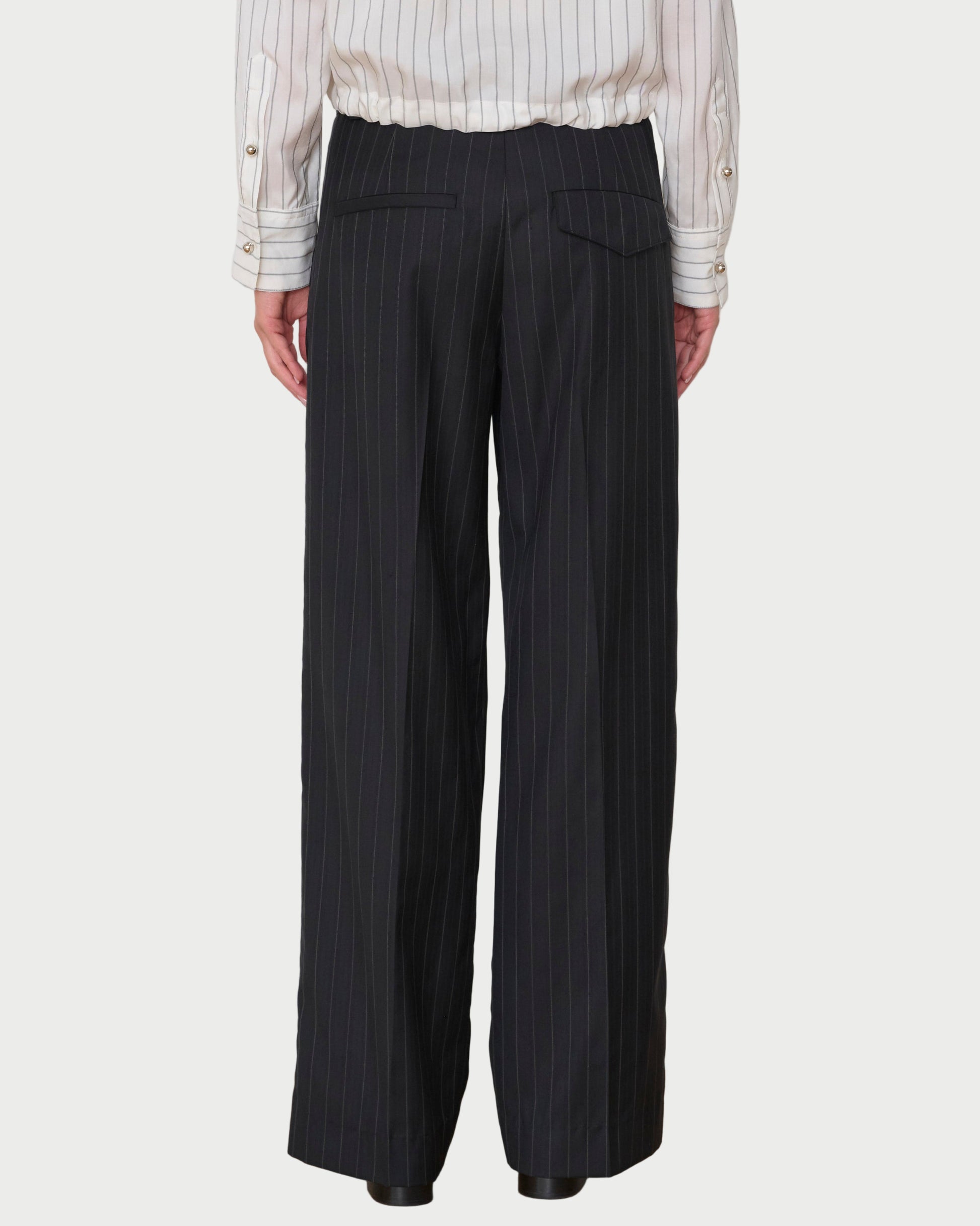Person wearing black pinstripe pants and a white shirt against a white wall.