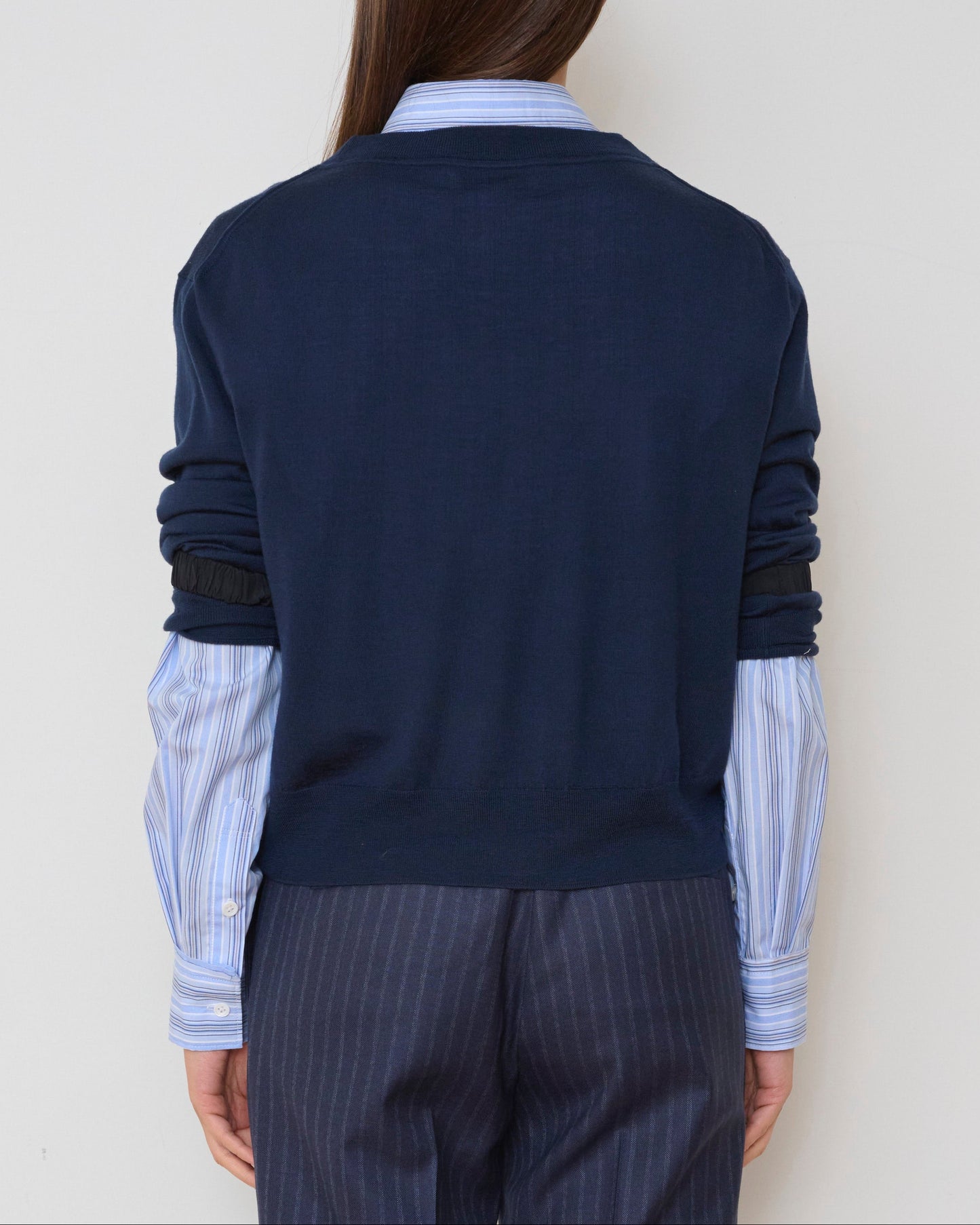 Person wearing a navy sweater over a striped shirt with a plain background