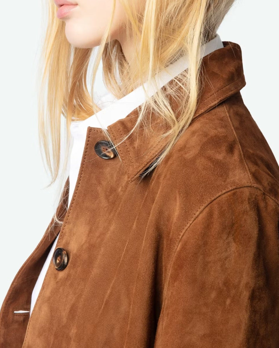 A person with long blonde hair wears a white collared shirt under the Lessa Suede Jacket by Zadig & Voltaire. The image is cropped to show just the lower half of their face and upper body.