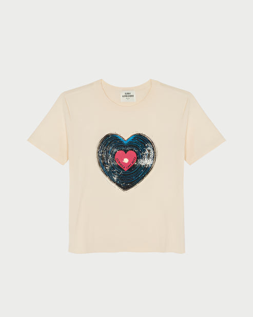 The Record Everyday Tee by Sunny Somewhere is a beige short-sleeve top featuring a large sequin heart inspired by a heart-shaped record, with a blue outer heart and pink center on the front.