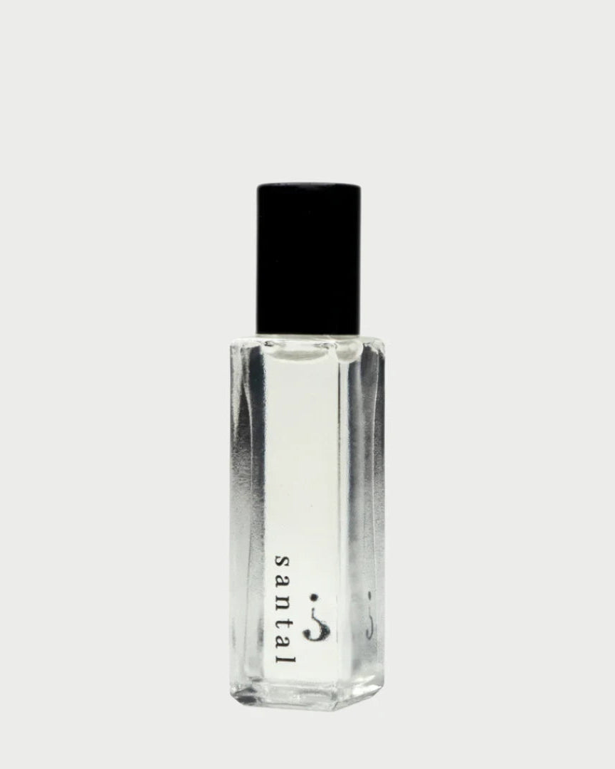 A clear rectangular bottle with a black cap from Riddle Oil exudes an exquisite fragrance. The label on this 8ml "Riddle Oil: Santal" perfume features a minimalist design on the lower part of the bottle, showcasing its sandalwood-infused santal scent against a pale gray background.