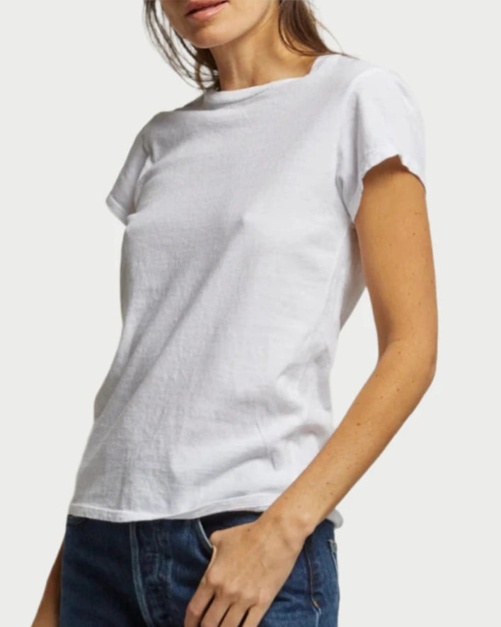 A woman stands against a light background wearing the Sheryl Basic Tee by perfectwhitetee and blue jeans. Her face is partially out of frame, and one hand rests on her hip.