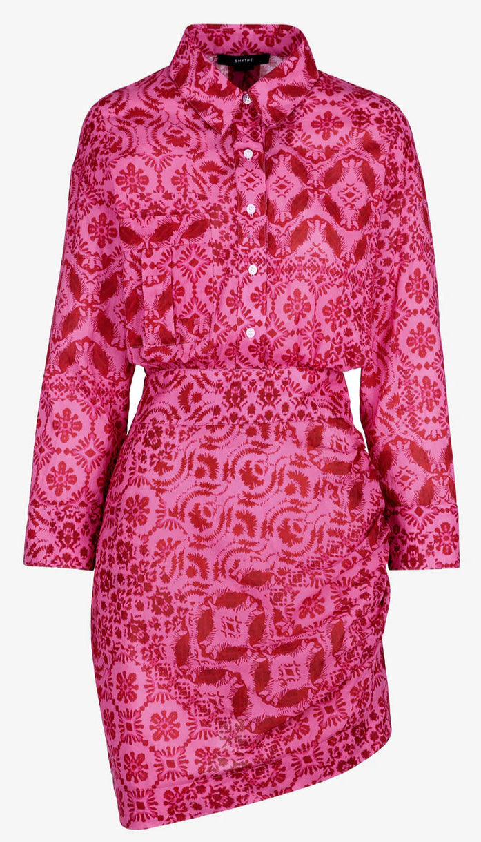 The Smythe Mini Shirt Dress is a bright pink, long-sleeve button-up featuring a collared neckline, red floral and geometric print, and a fitted asymmetrical skirt.
