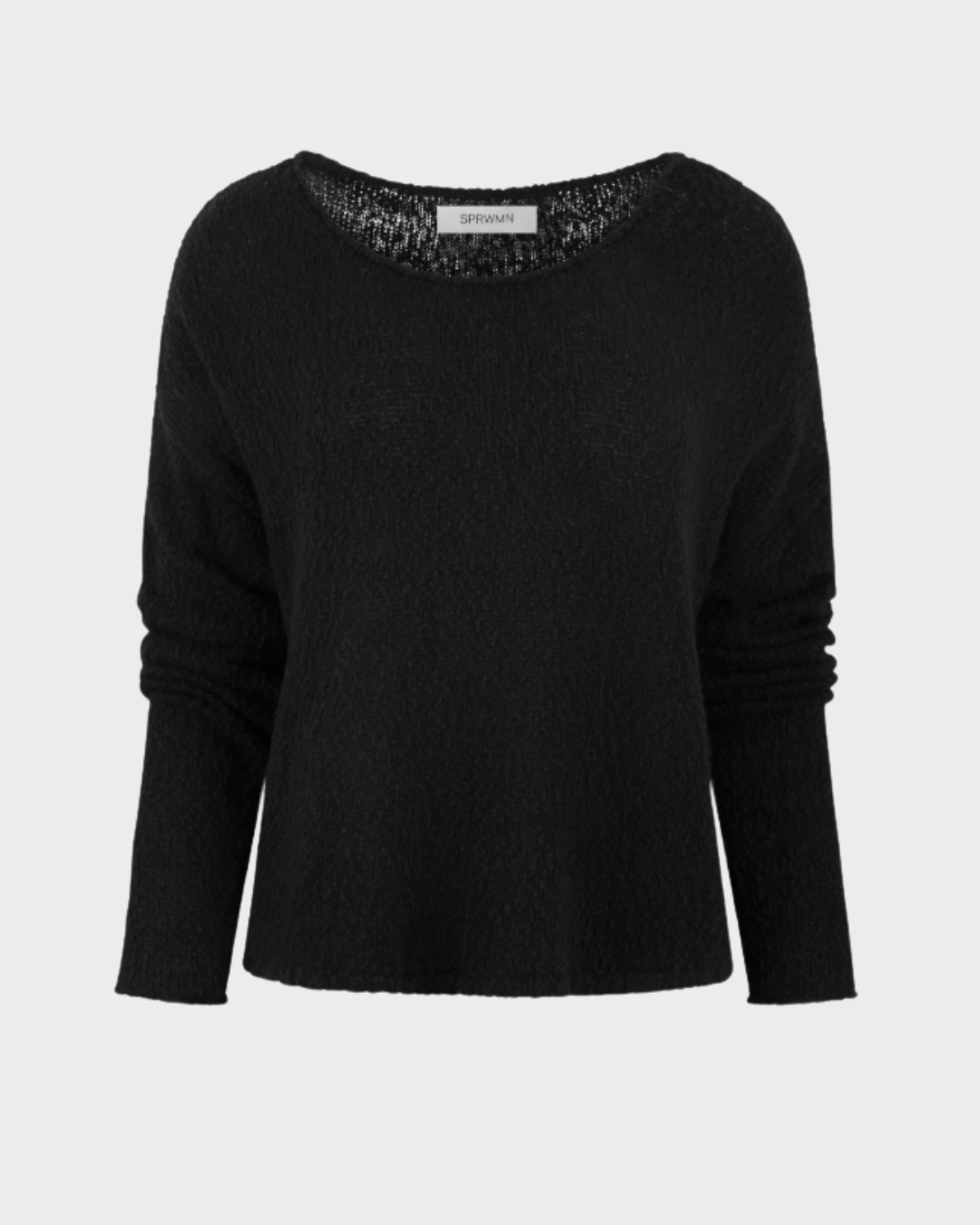 The SPRWMN Off Shoulder Sweater by SPRWMN features a loose fit, plain black cotton bouclé fabric with a slight texture and wide round neckline, shown against a light gray background.