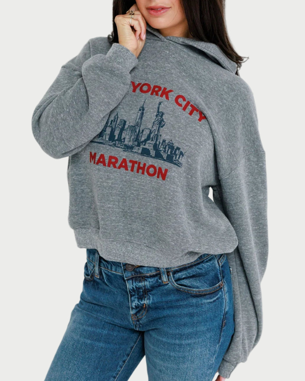 Woman wearing a gray hoodie with 'New York City Marathon' design against a white background