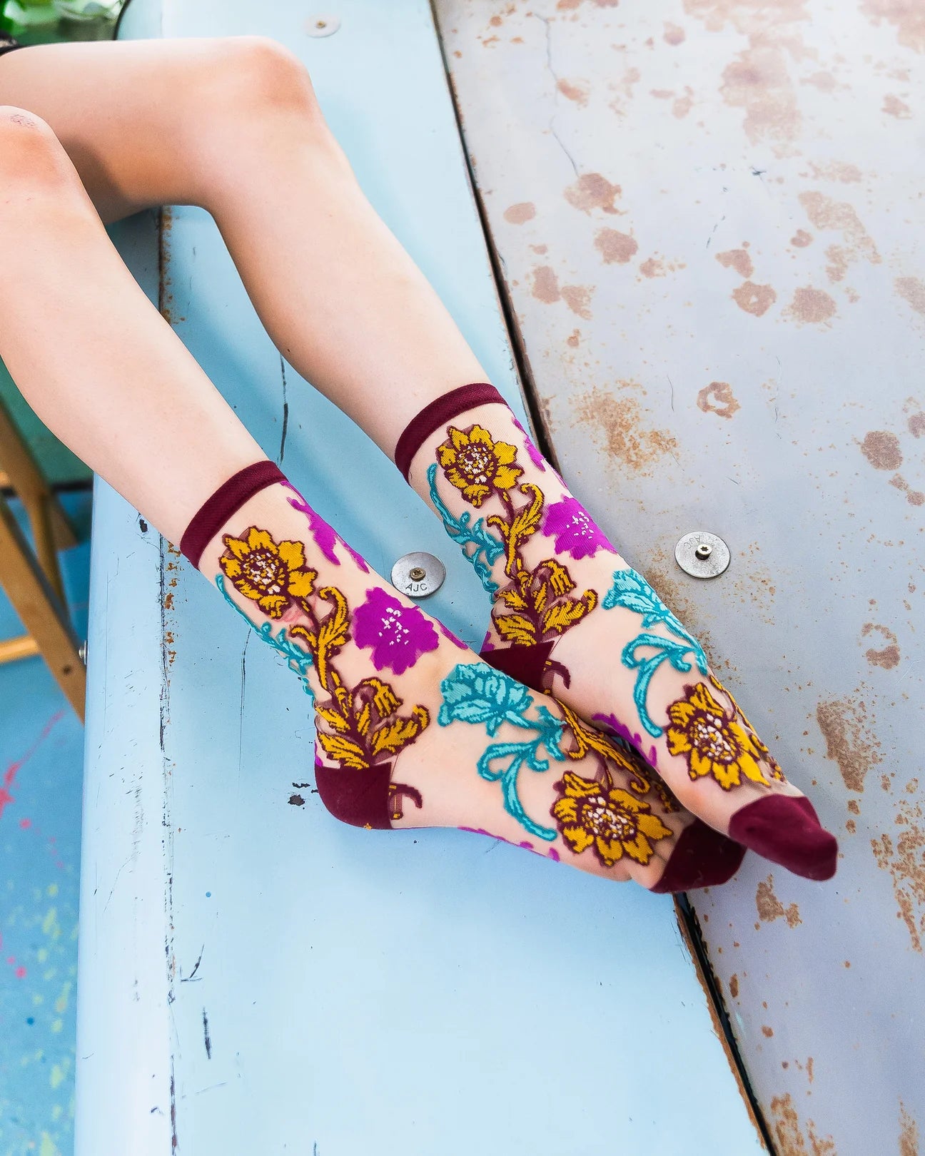 Colorful floral-patterned socks on a person's feet with a rustic wooden floor background.