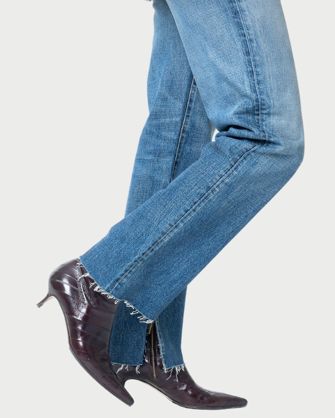 A person wears Moussy Massapequa Straight Leg Jeans and dark pointed-toe heeled boots, sitting with one leg crossed over the other against a white background.