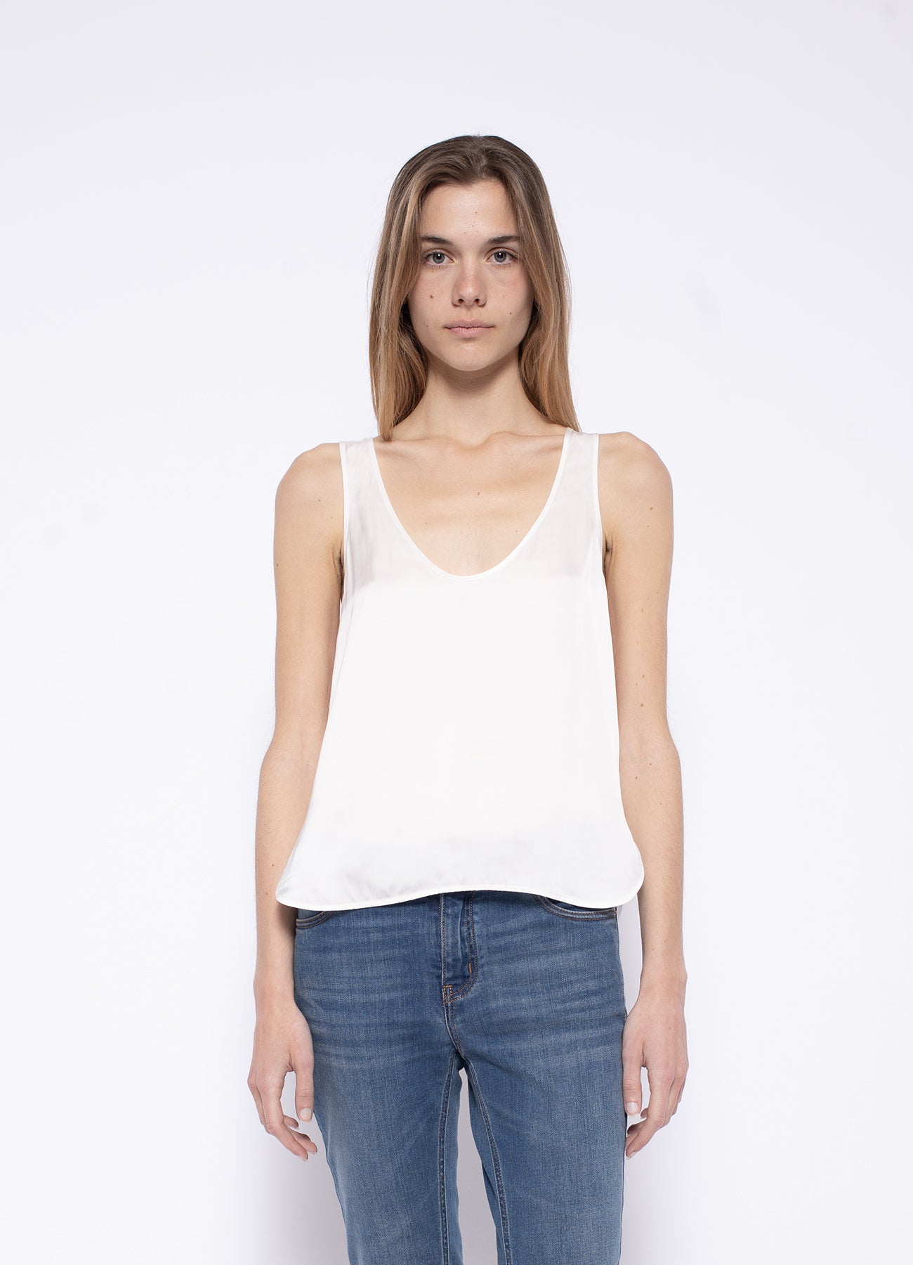 A person with long hair is wearing a Zadig & Voltaire Satin Cami and blue jeans, standing against a plain white background.