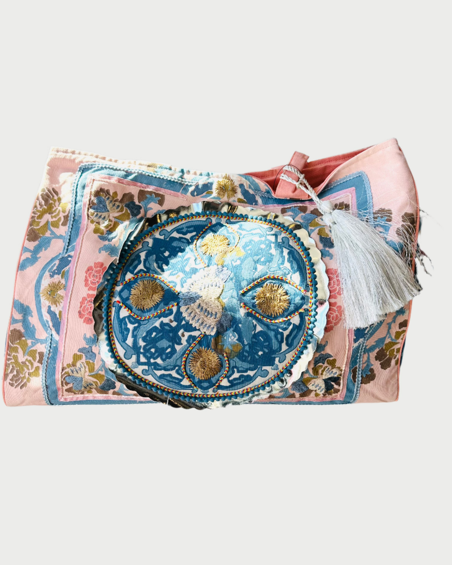 The DEBBIE KATZ Boho Bag features a vibrant embroidered design with a central circular blue and gold motif, surrounded by pink floral patterns on a pink base. It includes a white tassel on top, ideal for enhancing any outing.