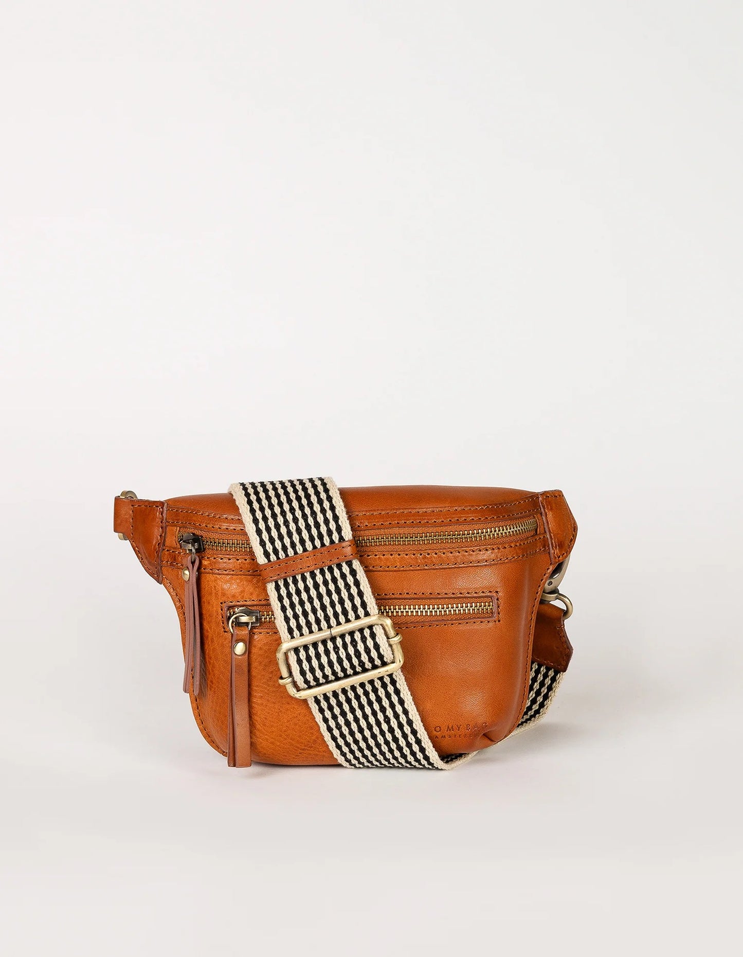 The Beck's Bum Bag in Cognac by O MY BAG features a front zipper pocket and a wide, black-and-white striped adjustable strap, shown against a plain white background.
