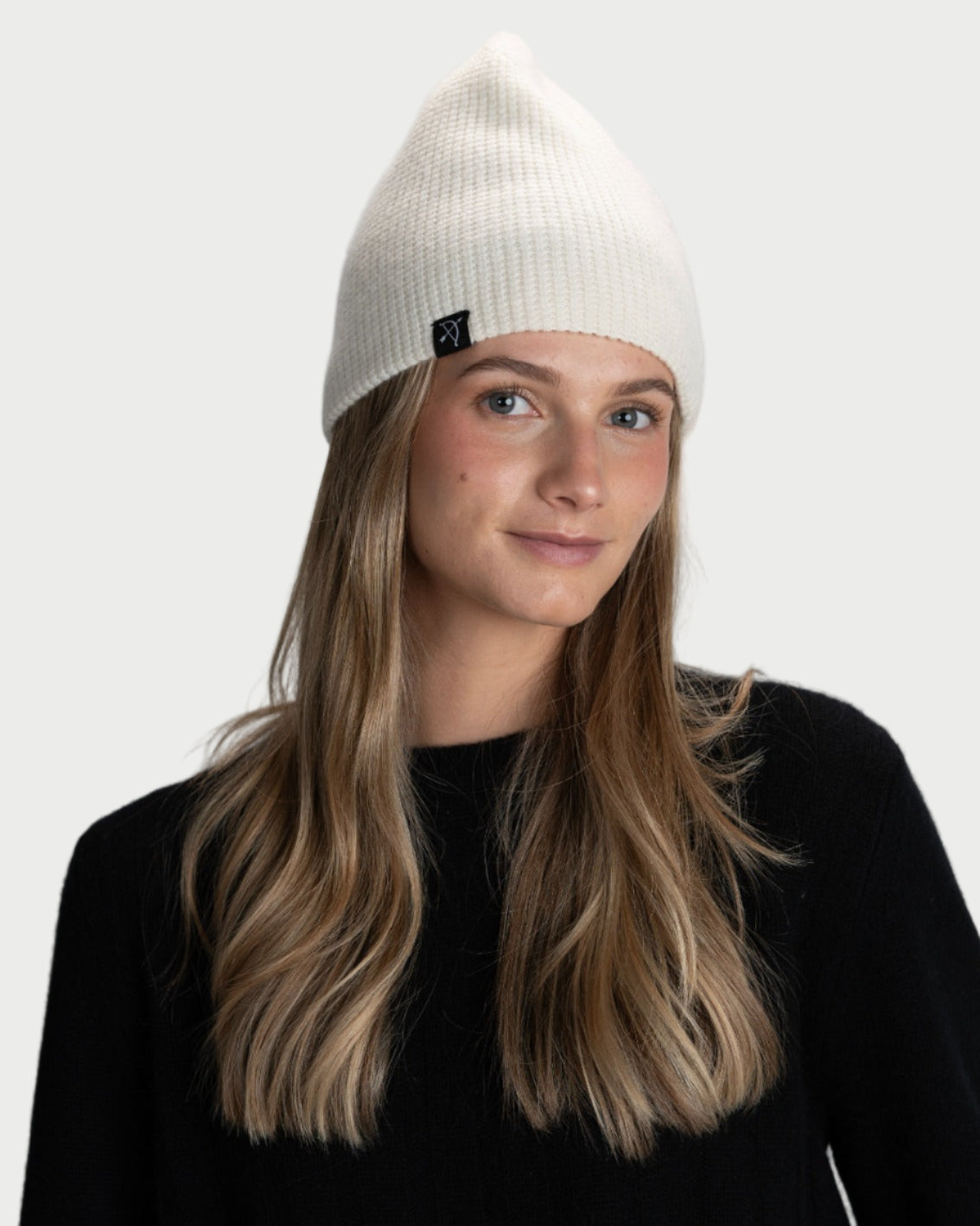 Person wearing a white beanie with a brand logo on a gray background