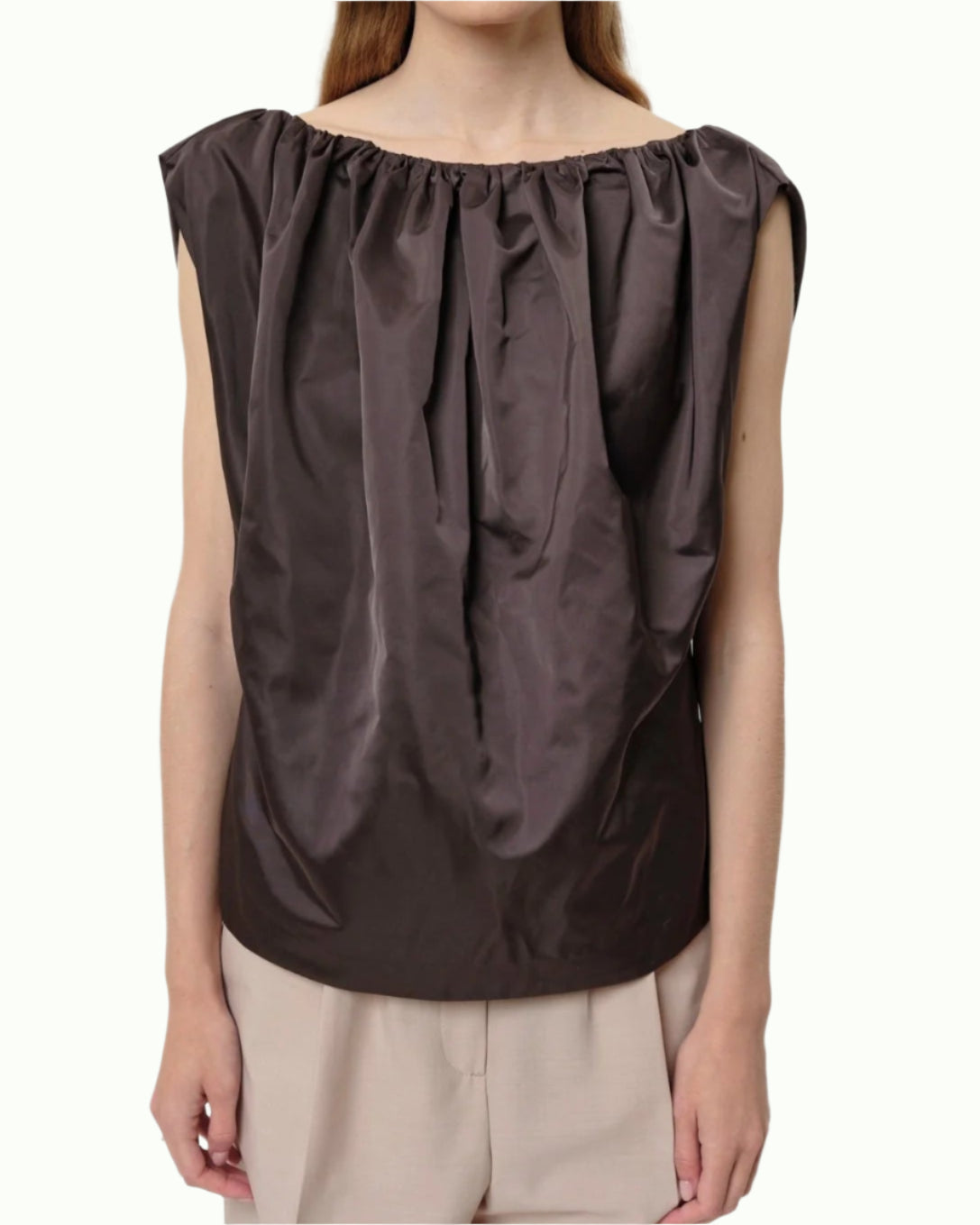 A person wears the Herskind Martina Top, a dark brown sleeveless style with a gathered neckline, paired with beige pants and shown waist up against a light background—an ideal choice for elevated cocktail attire.
