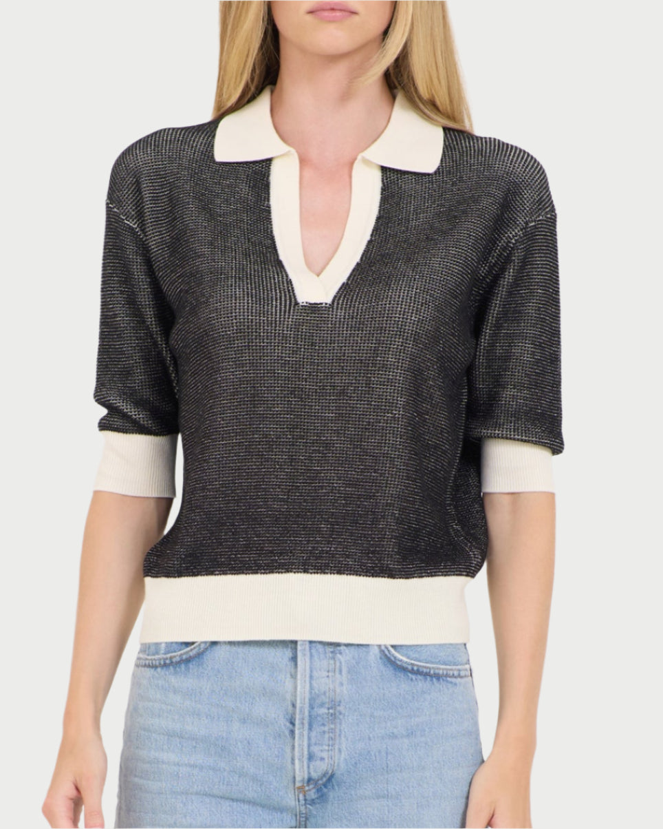 Someone sports a chic look, wearing a black knit One Grey Day Carmela Top, featuring a stylish white collar and cuffs. The short-sleeved V-neck pairs perfectly with light blue jeans, while their face remains out of view.