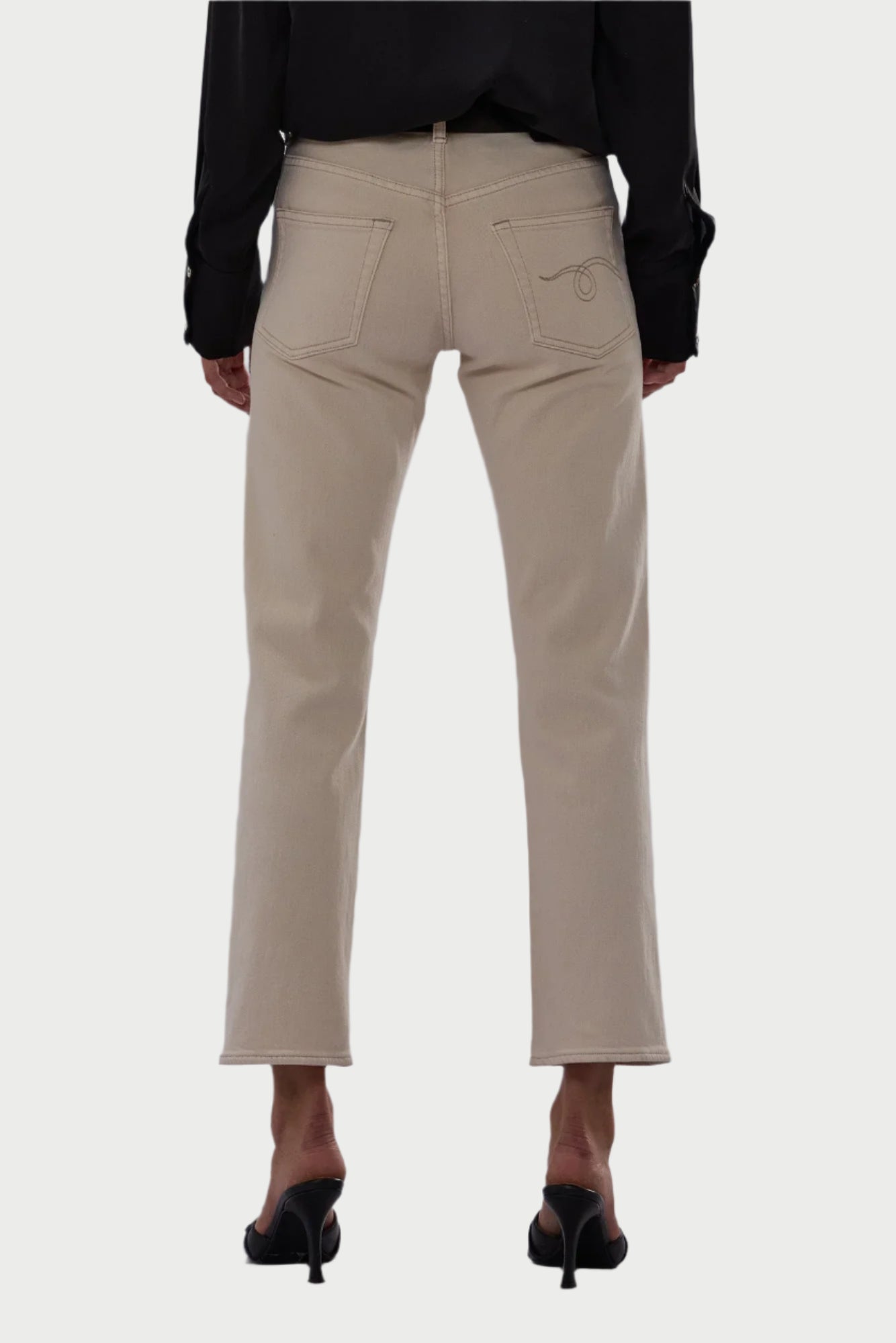 A person is shown from the back wearing R13 Romeo Jean in Ecru by R13, featuring straight legs, visible back pockets, and white stitching. The jeans are made from Japanese comfort stretch denim and paired with black heeled sandals.