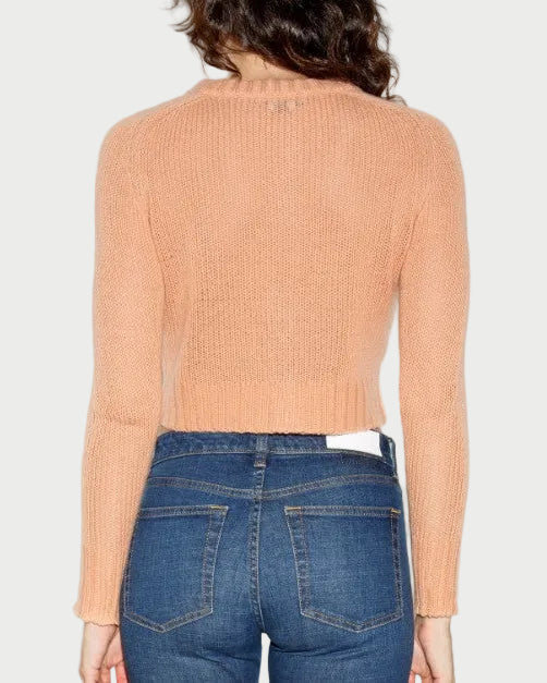 Person wearing a peach ribbed sweater and blue jeans on a light gray background