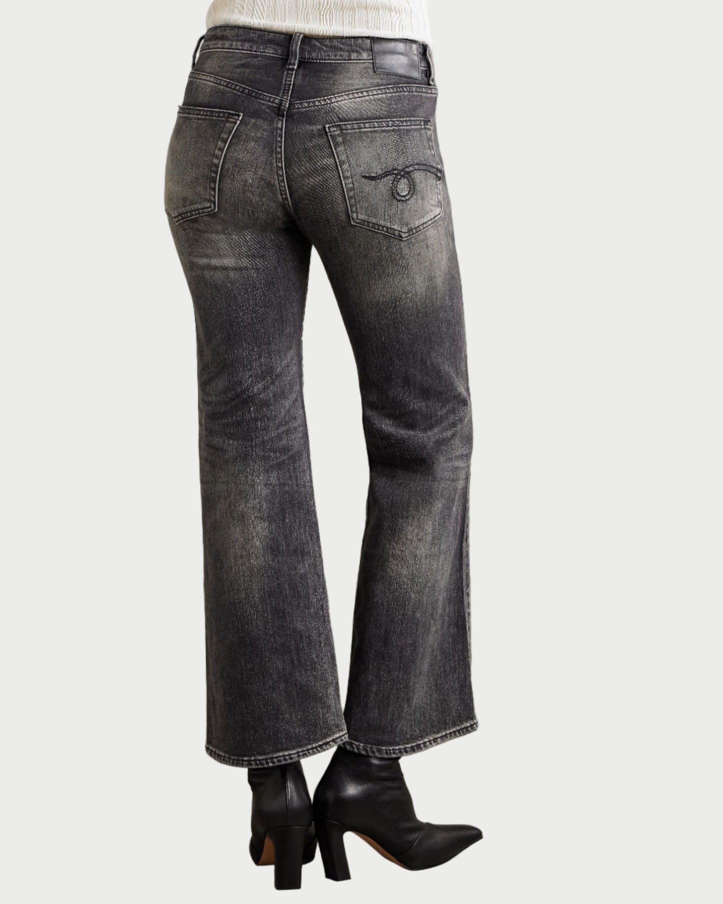 Person wearing black flared jeans and black shoes on a neutral background