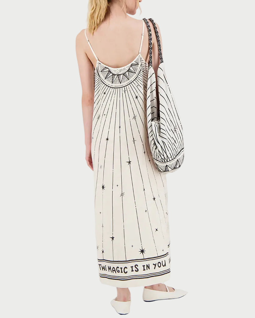 Woman wearing a long dress with star patterns and text, carrying a matching bag on a white background