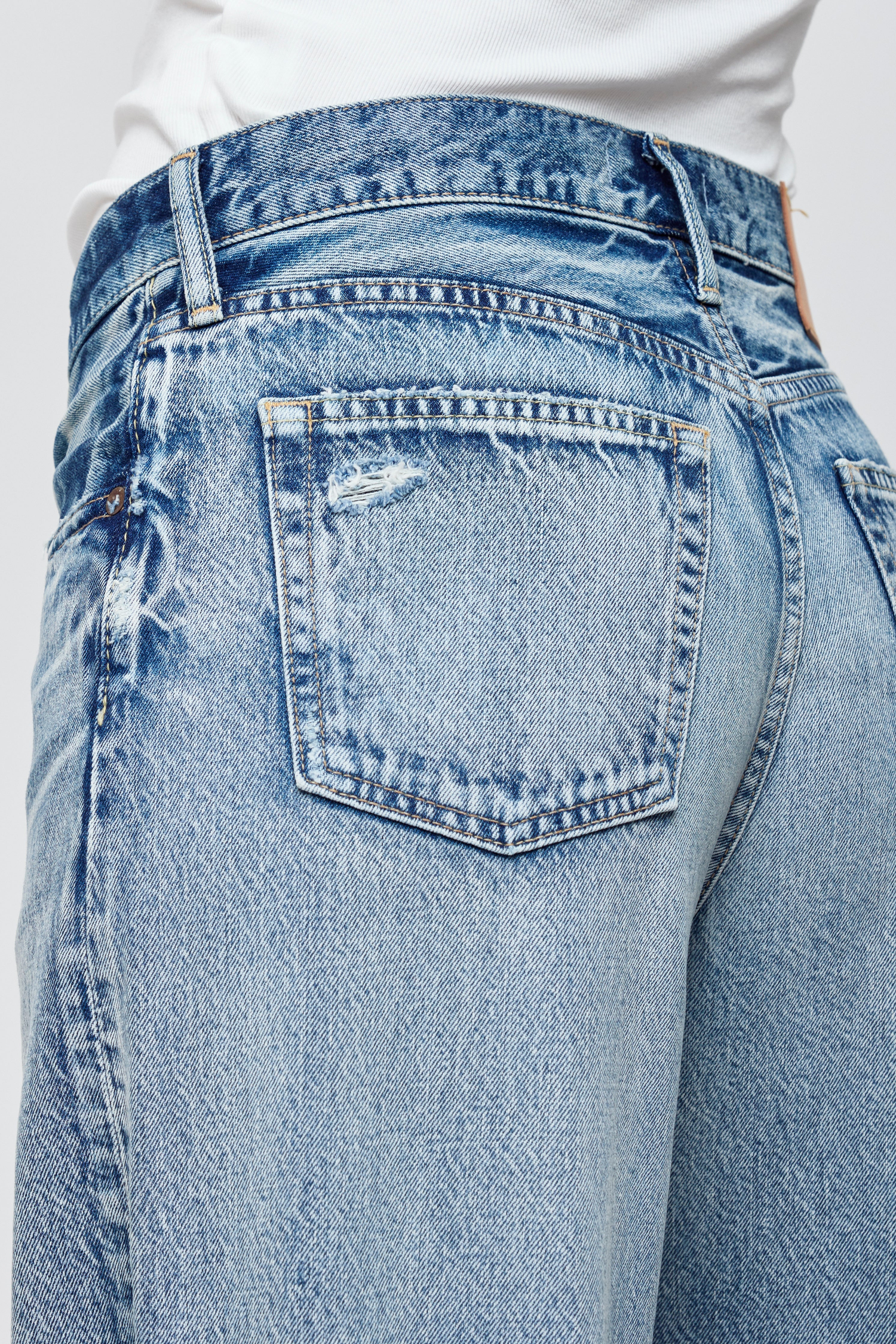 A person wearing high-waisted, wide-leg light blue jeans with a faded wash, standing against a plain light background and framed by a thick dark blue border.