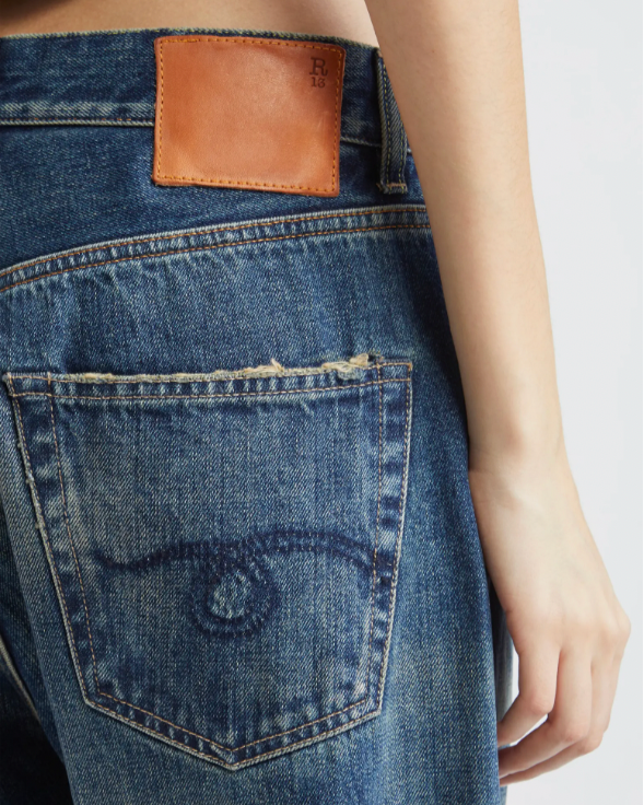 Person wearing loose-fitting, cuffed blue jeans with a faded wash and black boots, shown from waist to ankles against a white background with a blue border.
