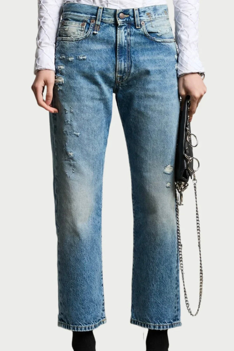Person wearing distressed blue jeans and a white long-sleeve shirt, holding a black clutch with a silver chain in one hand.