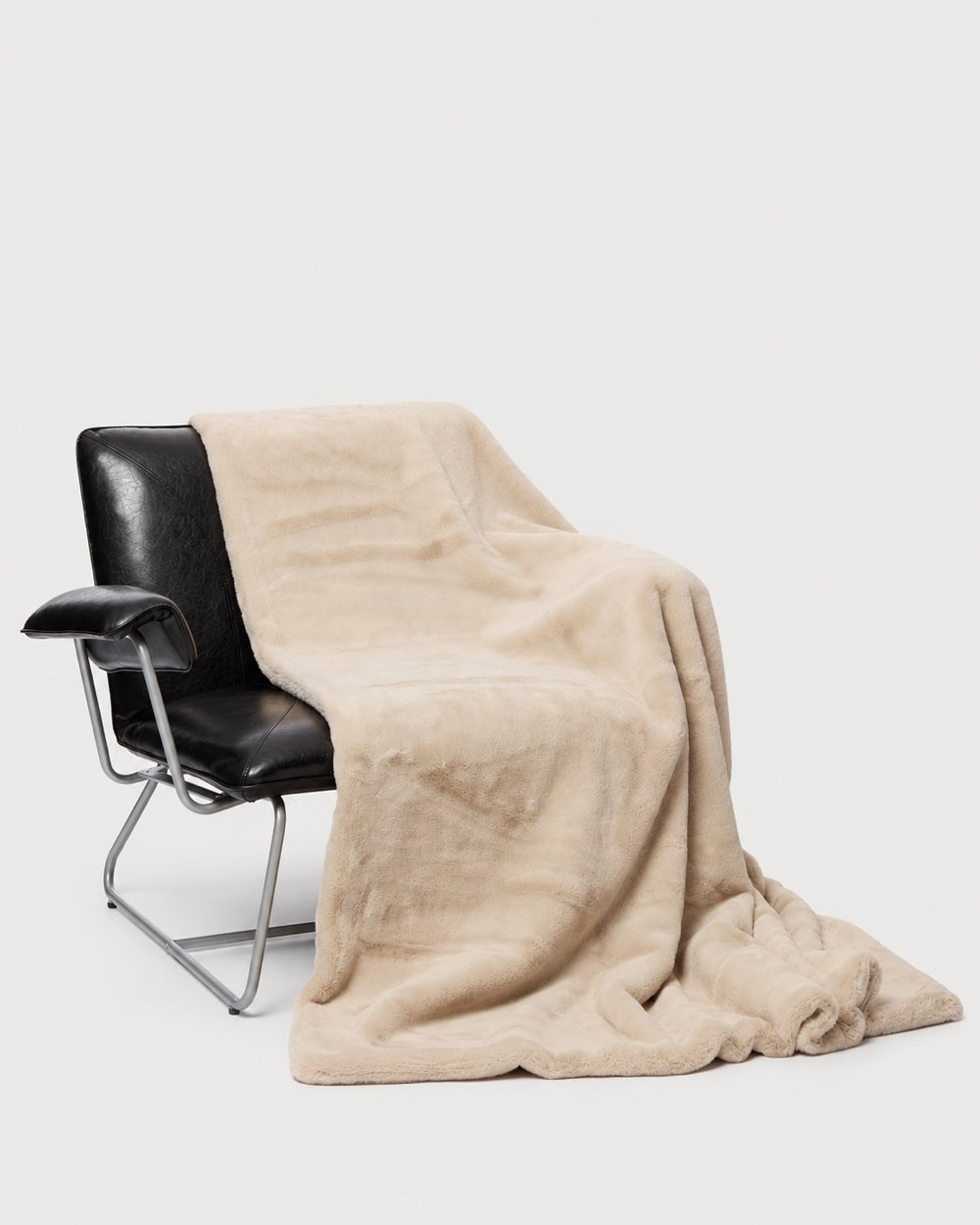 APPARIS Brady Blanket in Latte draped over a black lounge chair