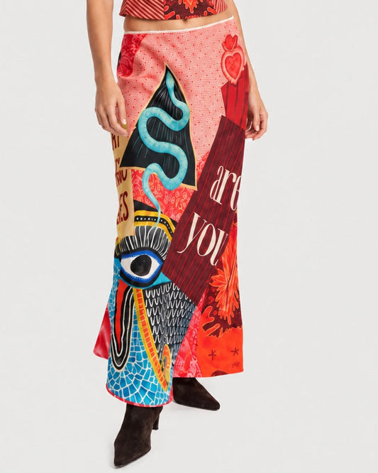 A person wearing a ME369 Blakely Slip Skirt Red Aura, a bias-cut skirt with a vibrant collage of red, pink, and blue abstract patterns, including an eye motif and the text “are you.”