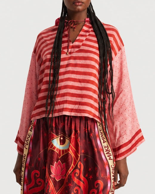 A ME369 Mei Cropped Hoodie Red Aura, featuring red stripes, a drawstring, and wide sleeves, worn over a skirt with an eye and lotus flower graphic.