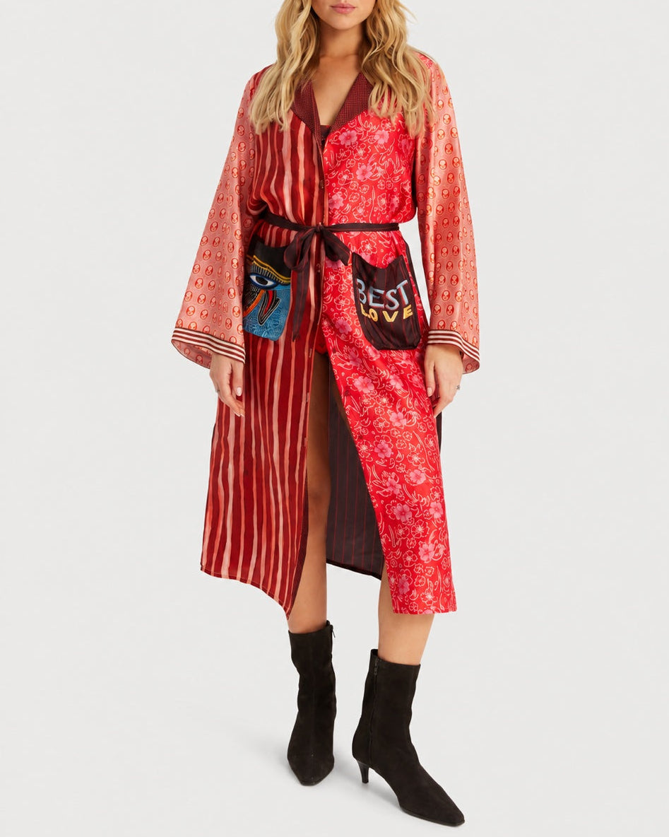 A long, red ME369 Nova Kimono Dress with a multi-patterned Aura print, featuring a front tie closure, large graphic patch pockets, and long sleeves, worn with black ankle boots.