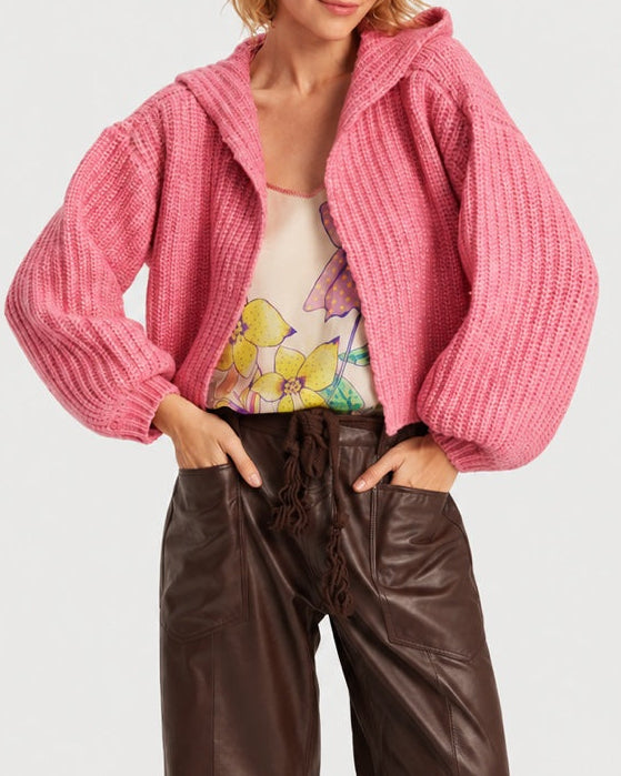 A bright pink, chunky ribbed knit ME369 Romi Hoodie Fuchsia worn over a floral camisole and dark brown trousers.