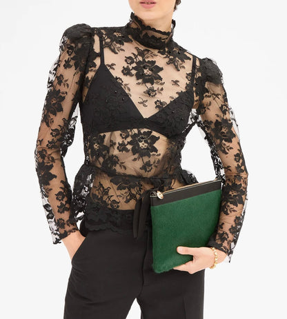 A person holding a Clare V. Flat Clutch Bottle Green, featuring a textured front and black trim.