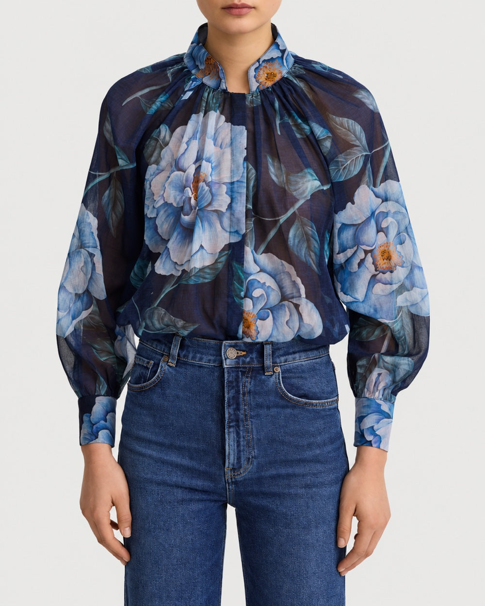 A navy blue Smythe Gathered Blouse Navy Floral with a high neckline, long sleeves, and a large blue floral print, worn tucked into blue jeans.
