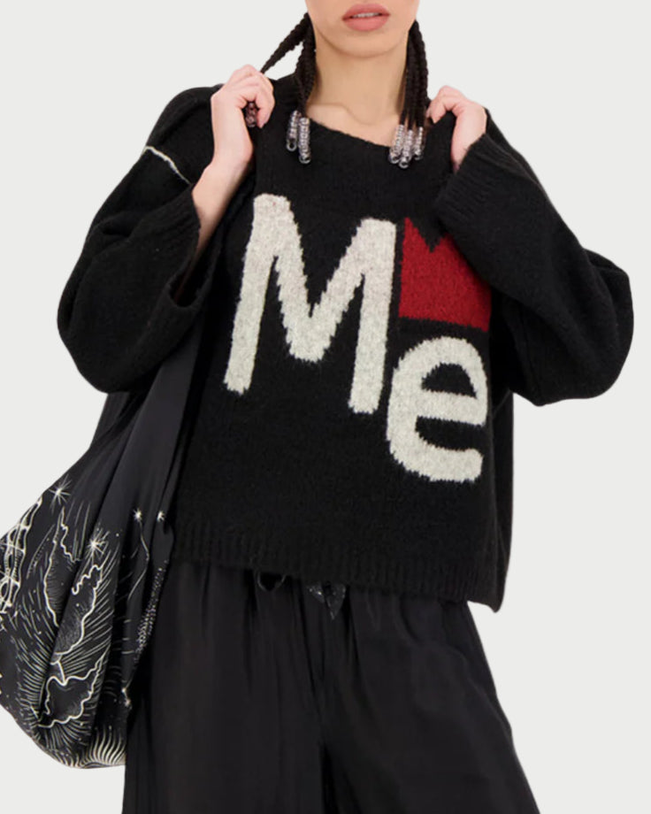 Person wearing a black sweater with 'Me' text, holding a patterned bag on a white background