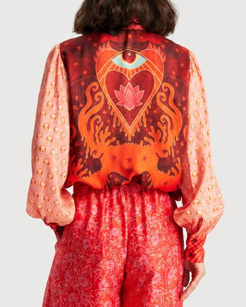 A person seen from behind wearing a red ME369 Sola Puff Sleeve Blouse Red Aura, featuring an all-over print of faces on the balloon sleeves and an eye and lotus graphic on the back.
