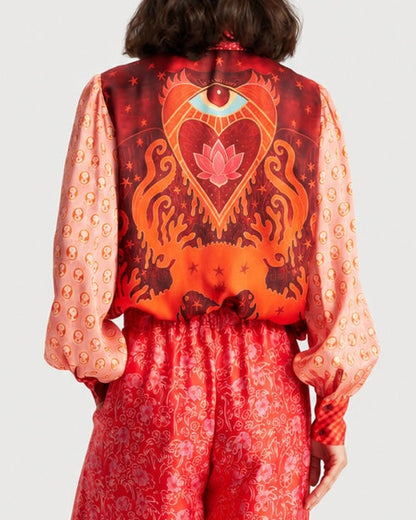 A person seen from behind wearing a red ME369 Sola Puff Sleeve Blouse Red Aura, featuring an all-over print of faces on the balloon sleeves and an eye and lotus graphic on the back.