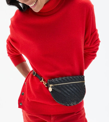 A person wearing a red turtleneck sweater and a black handwoven leather Clare V. Petite Fanny Black with a gold zipper and circular pull.