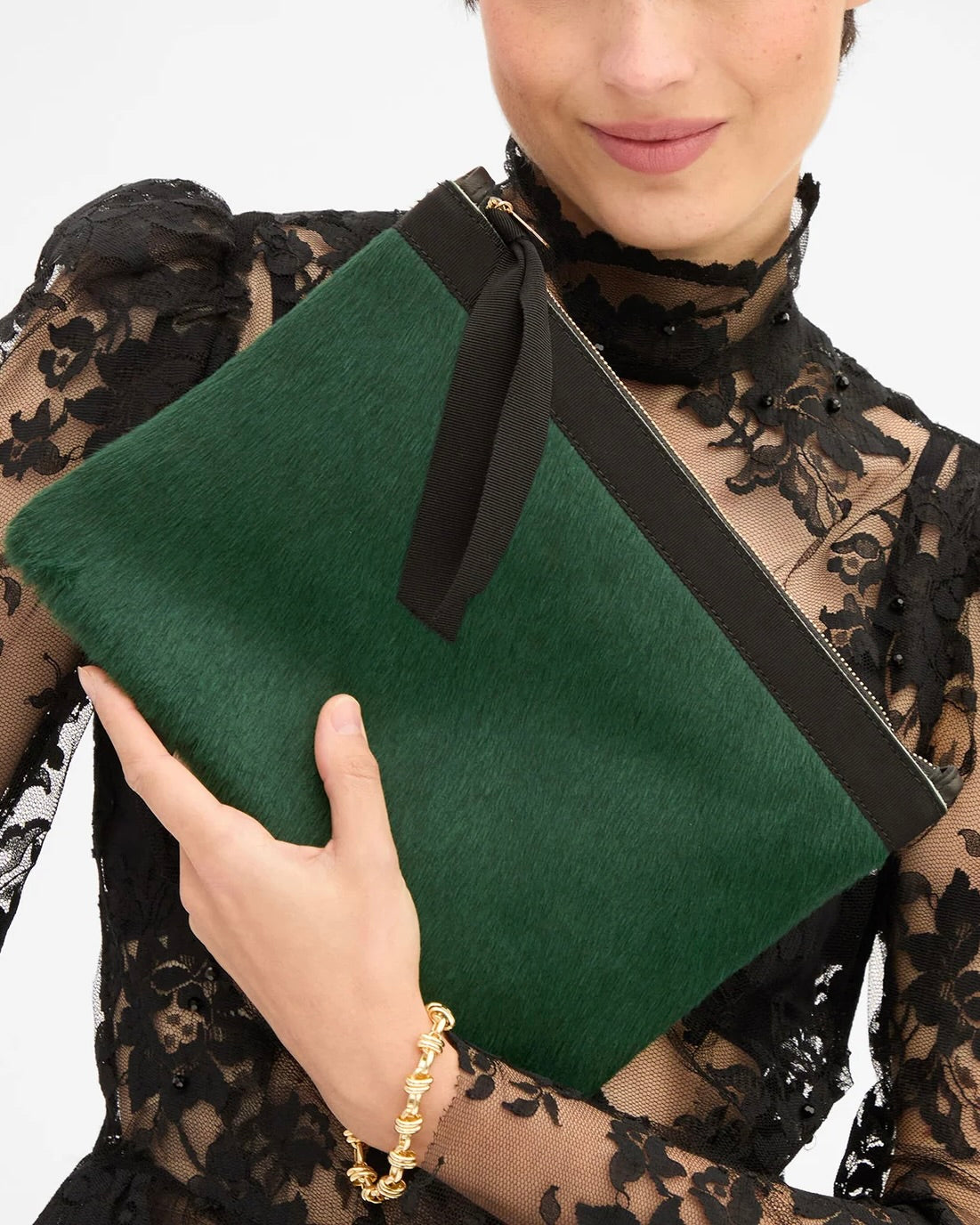 A person holds a flat, bottle green Clare V. Flat Clutch Bottle Green with a black zipper and a black ribbon pull.