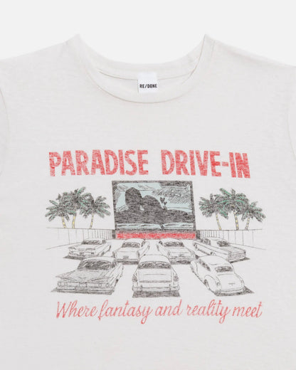 The Drive In Tee by RE/DONE is a white cropped vintage shirt with a drive-in theater graphic—cars, palm trees, and “PARADISE DRIVE-IN” plus “Where fantasy and reality meet.” Inspired by the iconic Paradise Drive In Tee.