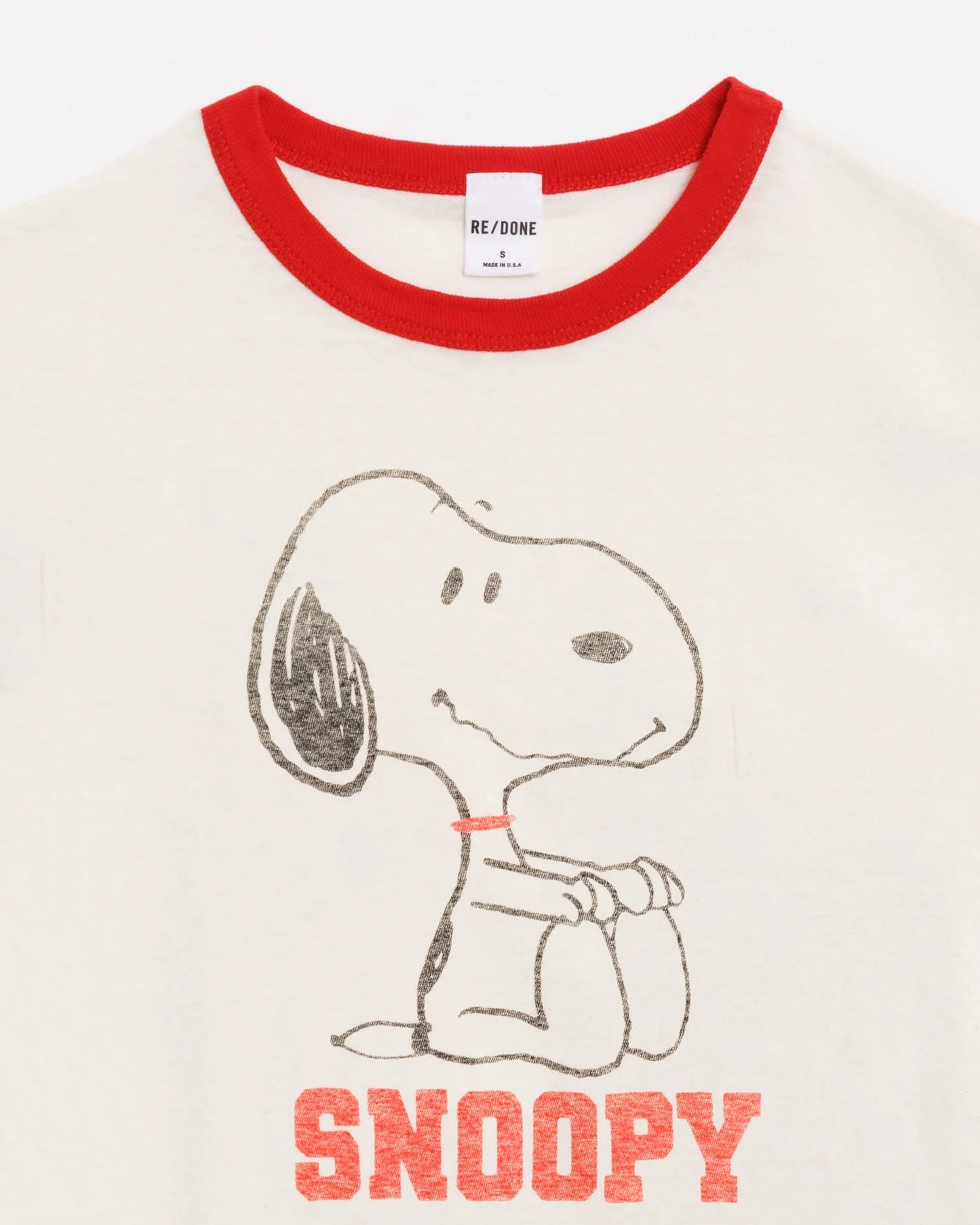 The RE/DONE Snoopy 60s Slim Ringer Tee is a cream-colored vintage-style ringer tee with a red collar, featuring Snoopy sitting and “SNOOPY” in bold red letters below.