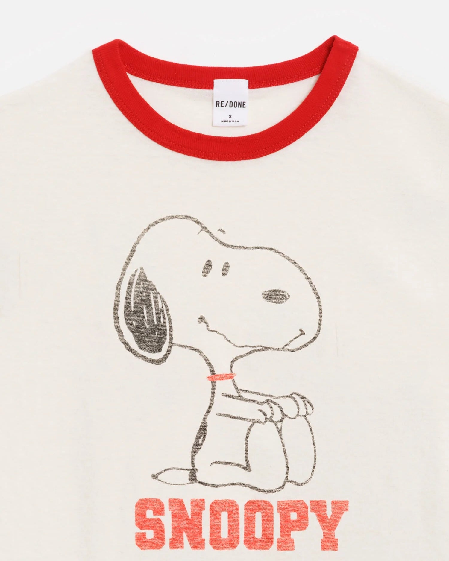 The RE/DONE Snoopy 60s Slim Ringer Tee is a cream-colored vintage-style ringer tee with a red collar, featuring Snoopy sitting and “SNOOPY” in bold red letters below.