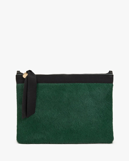 Clare V. Flat Clutch Bottle Green in a flat, rectangular shape made of bottle green hair-on leather with a black top border and a black ribbon tied to the gold zipper pull.