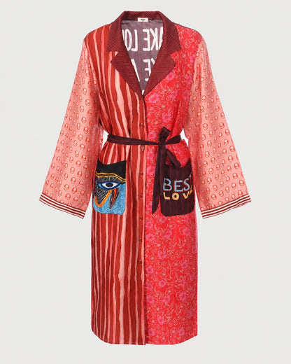 ME369 Nova Kimono Dress Red Aura with long sleeves in mismatched red patterns, featuring a waist tie, an eye graphic on one pocket, and the word “LOVE” on the other.