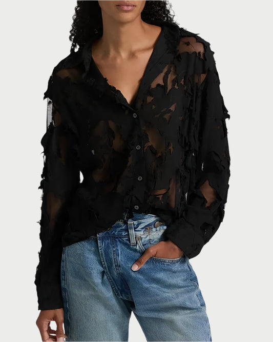 A person wearing the R13 Slim Abstract Print Shirt, featuring a sheer, distressed look with frayed details, styled over light blue jeans and standing with one hand in their pocket.