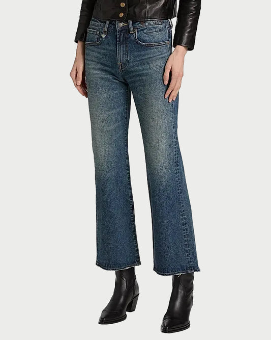 A person wearing blue denim flare jeans with a black leather jacket and black ankle boots, shown from the chest down on a plain white studio background.