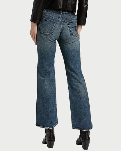 Rear view of a person wearing blue denim flare jeans with a black leather jacket and black ankle boots against a white background.