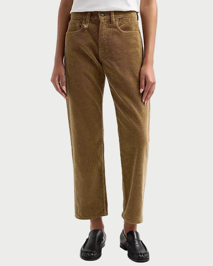 A model wearing a pair of brown corduroy cropped jeans with a white top and black loafers, shown from the waist down against a light gray studio background.