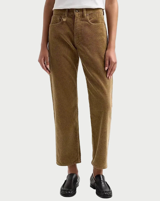 A model wearing a pair of brown corduroy cropped jeans with a white top and black loafers, shown from the waist down against a light gray studio background.